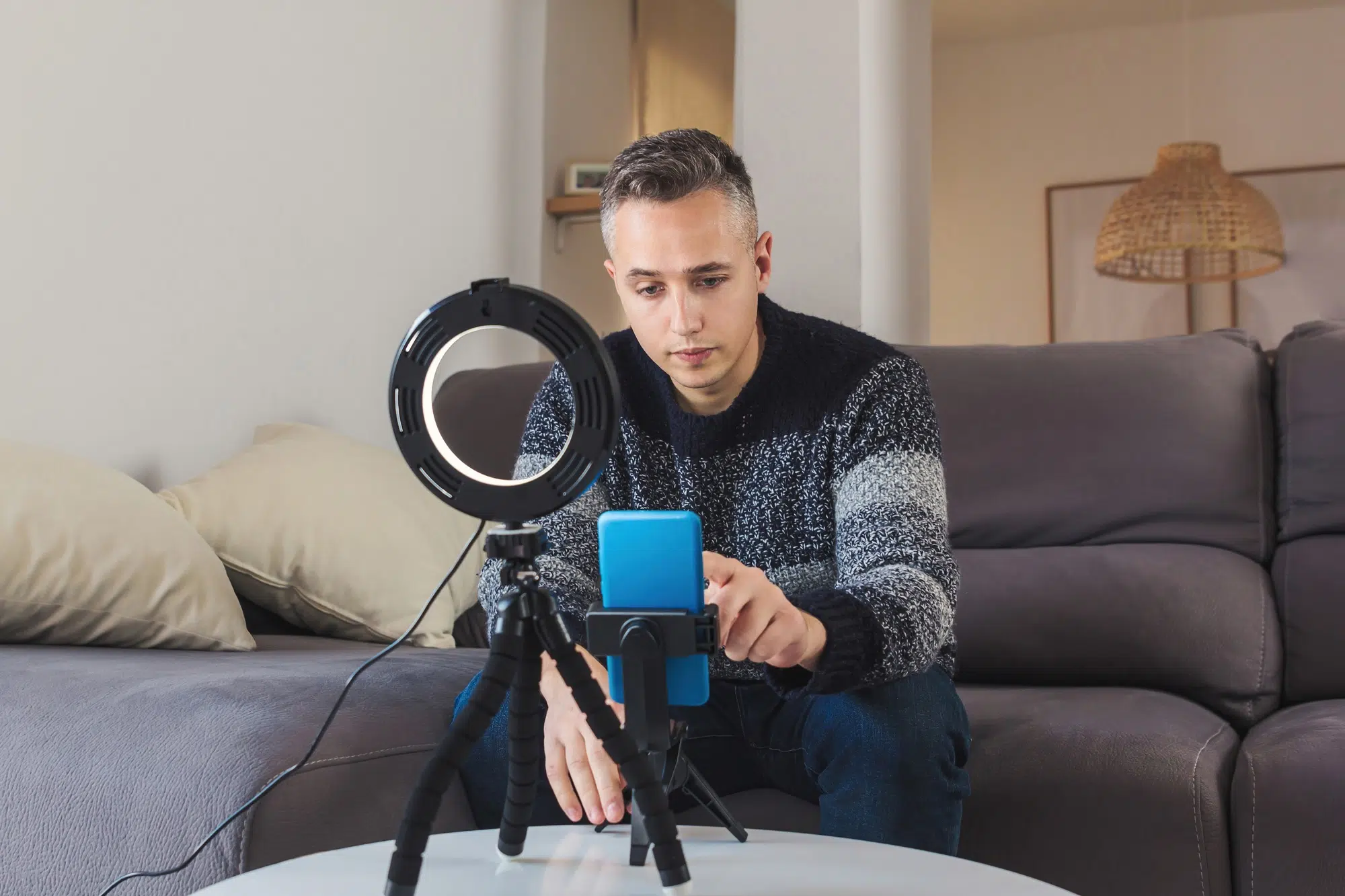 Young man influencer on sofa setting up mobile phone and lighting for vlogging or video call